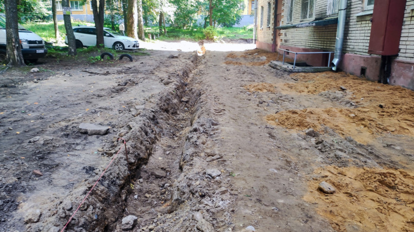 Траншея у входной группы с поручнями и водосточной трубой рядом с кучами песка