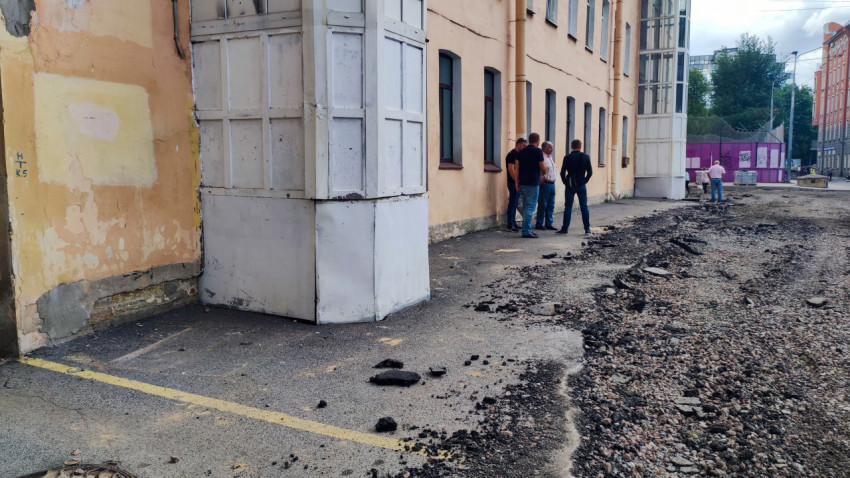 Разобранное асфальтовое покрытие у фасада здания и группа людей на участке дорожных работ во дворе