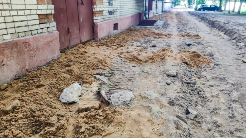 Земляные работы вдоль фасада многоквартирного дома с песчаной подсыпкой и разрытым грунтом