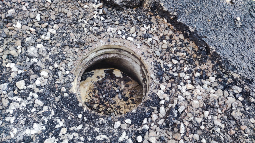Крупный план открытого колодца в асфальте с водой и щебнем после дорожных работ