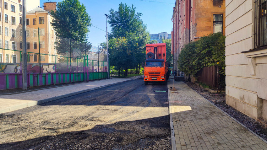 Оранжевый самосвал КамАЗ на ремонтируемом проезде с новым асфальтом и тротуарной плиткой