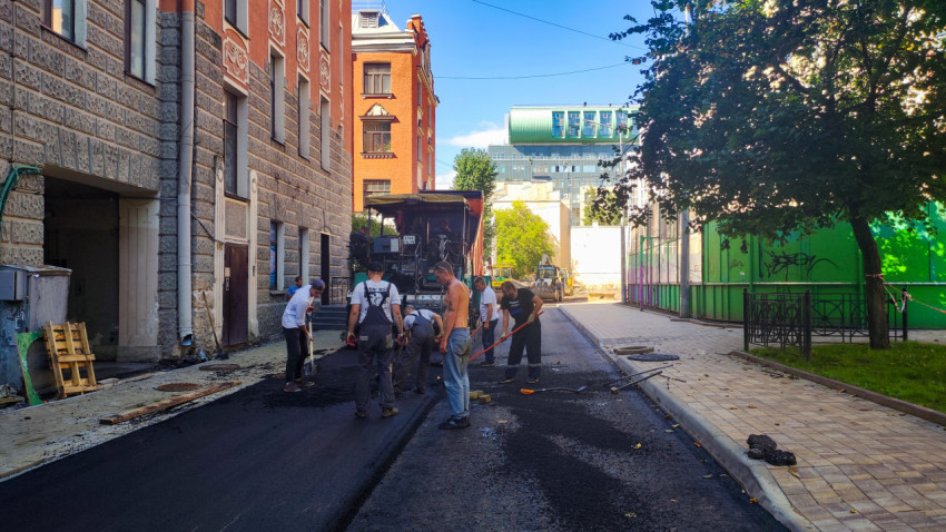 Бригада укладывает новый асфальт асфальтоукладчиком и лопатами на городской улице