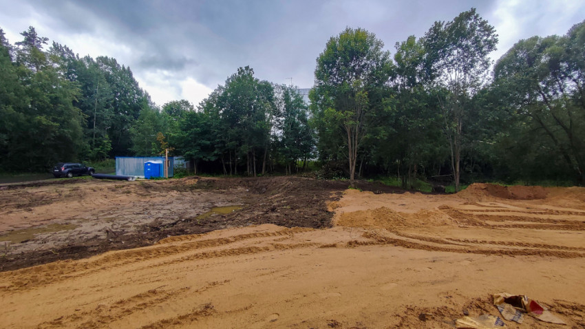 Песчаная строительная площадка в лесопарке с временными бытовками, техникой и водоотводом