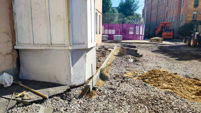 Установка бордюра на песчано-щебёночном основании рядом со штабелем плитки и грузовиком