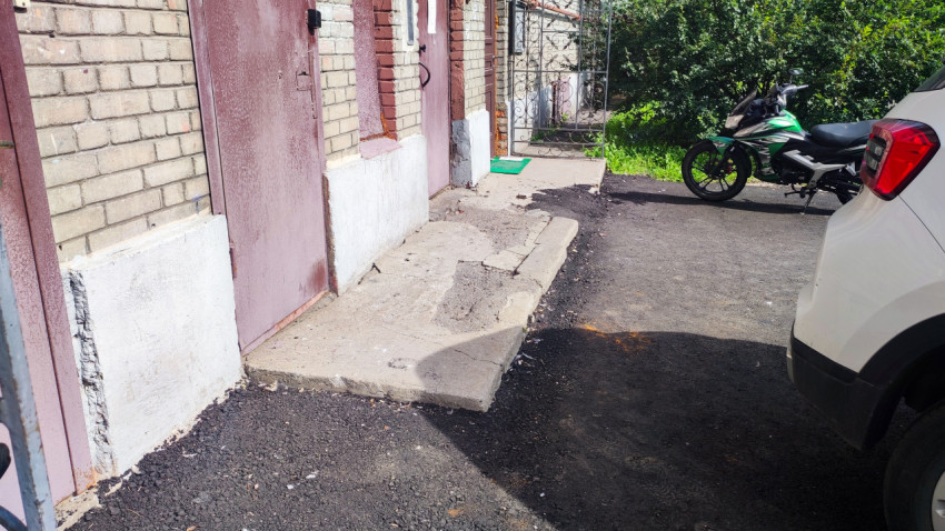 Дворовой проезд с новым асфальтом у кирпичного дома, припаркованным автомобилем и мотоциклом у входной площадки