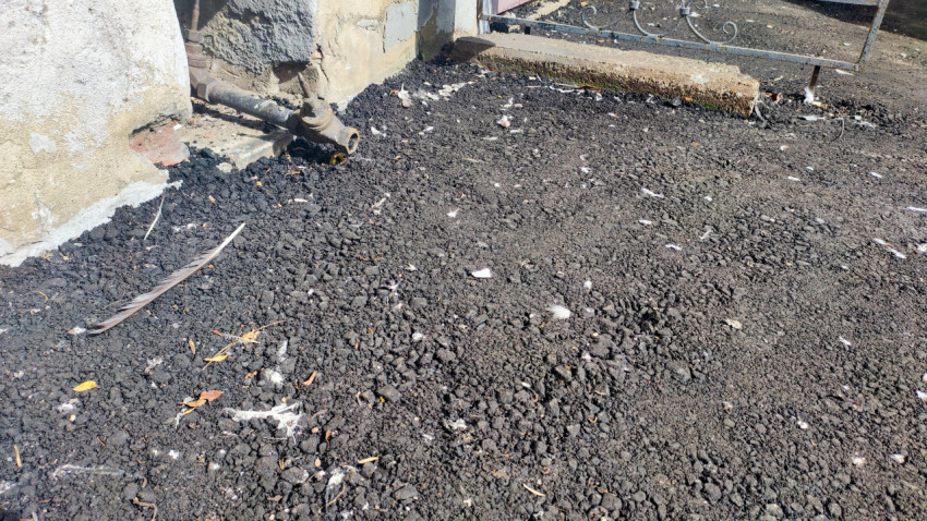 Крупный план свежего асфальта с щебёночной фракцией, листьями и мелким мусором у стены здания