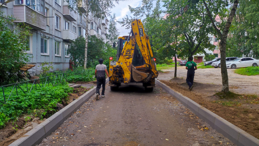 Экскаватор-погрузчик JCB 4CX и рабочие на дворовом проезде с установленными бордюрами