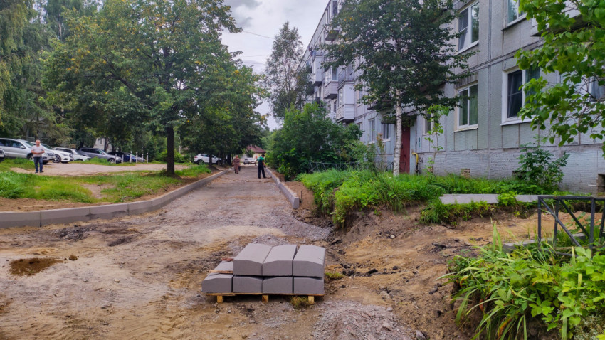 Паллет с бордюрным камнем на стройплощадке двора рядом с панельным домом и разрытым грунтом