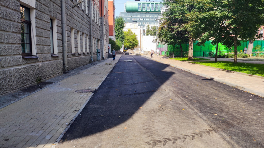 Свежий асфальт на внутриквартальной дороге рядом с тротуаром и зелёным ограждением