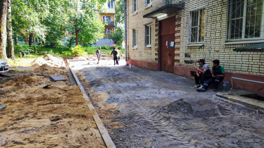 Рабочие у бокового входа кирпичного дома во время ремонта прохода и укладки бордюров