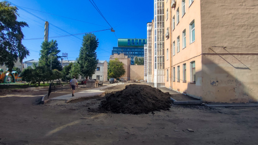 Куча грунта и разрытый двор с ограждением площадки на фоне жилых домов