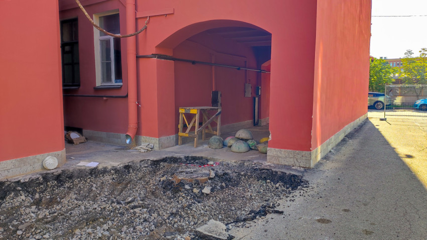 Раскопанный участок под аркой дома с временным ограждением и коммуникациями