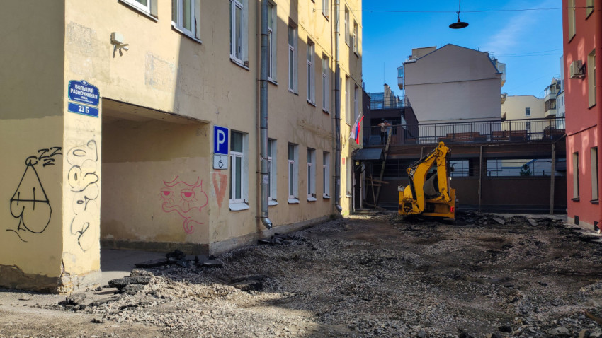 Мини-экскаватор и разобранный асфальт в узком дворовом проезде