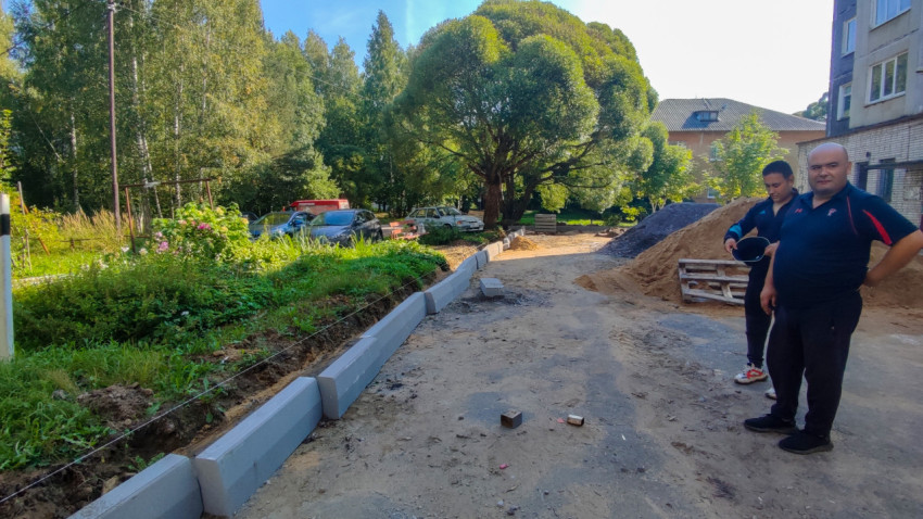 Монтаж бордюрного камня по шнуру во дворе рядом с кучами песка и щебня