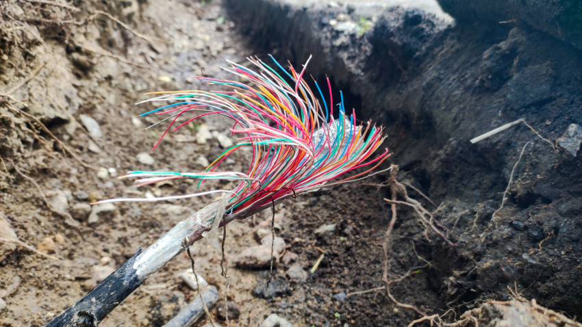 Пучок цветных жил повреждённого кабеля в грунтовой траншее крупным планом