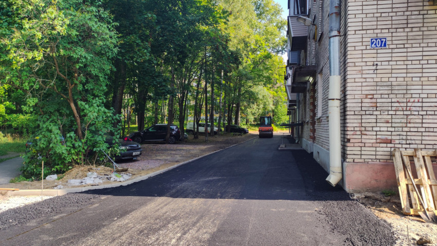 Свежий асфальт вдоль кирпичного дома тянется к дорожному катку в конце проезда