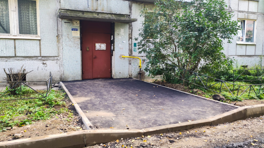 Новая асфальтовая площадка у подъезда с красной дверью, бордюрами и жёлтой газовой трубой
