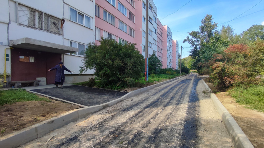 Дворовая улица вдоль длинного дома: новые бордюры, щебень и жительница на фоне ремонта
