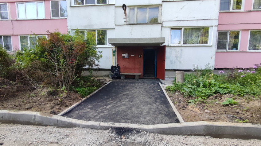 Подъезд панельного дома с козырьком и свежим асфальтом у входа