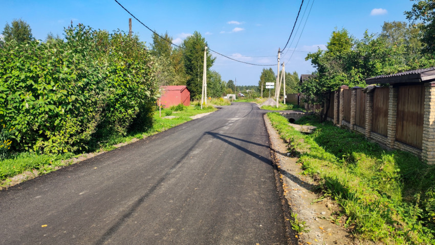 Асфальтовая улица в частном секторе с канавой, трубой-проездом и заборами вдоль дороги