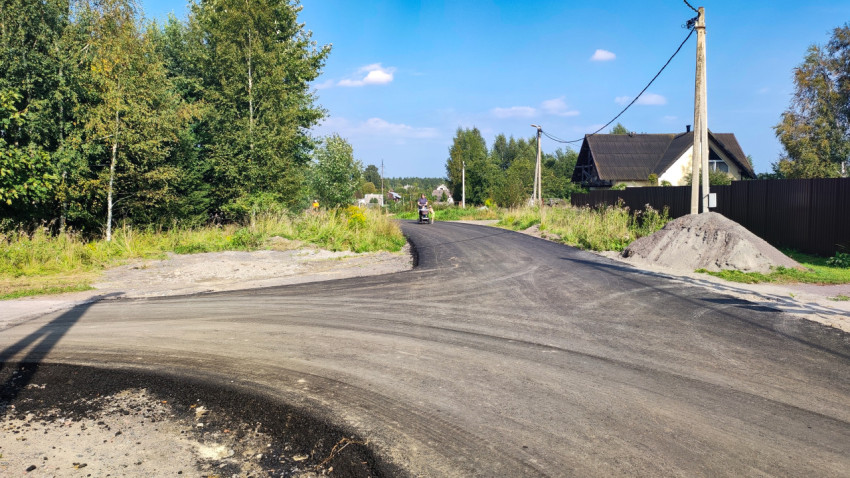 Перекрёсток с новым асфальтом, кучей песка у обочины и человеком с коляской вдали