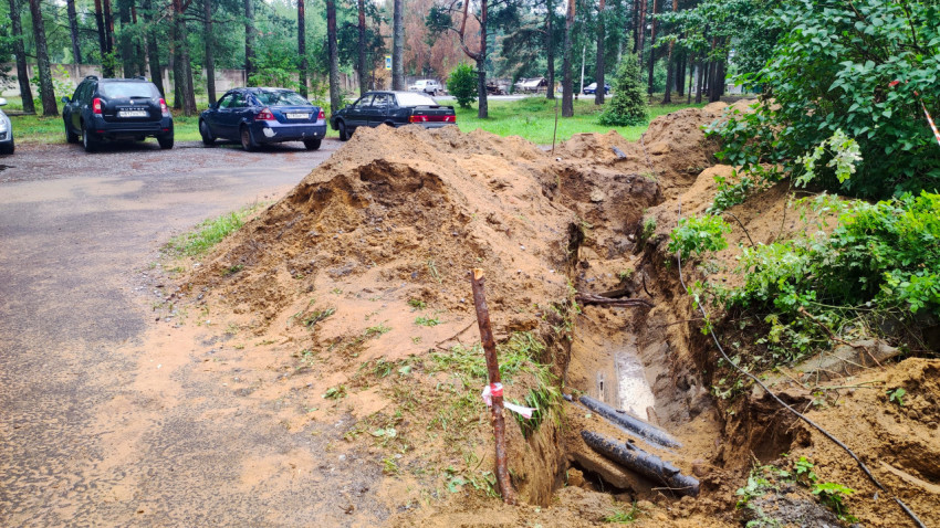 Раскрытая траншея с трубопроводом и кабелем на дворовой ремонтной площадке