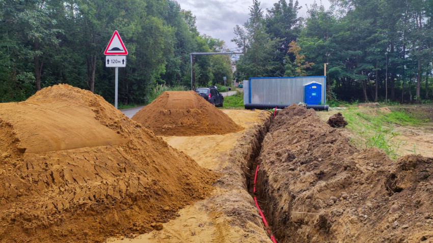 Дорожные работы у лесной дороги с траншеей, песком и предупреждающим знаком