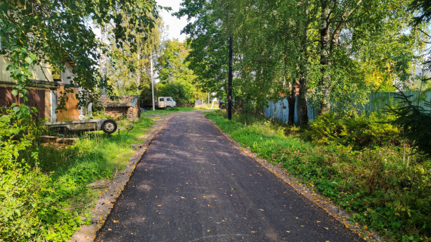 Тенистая деревенская улица со свежим асфальтом и припаркованным фургоном