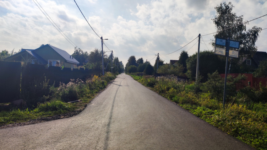 Прямая сельская дорога с заборами, домами и линиями электропередачи