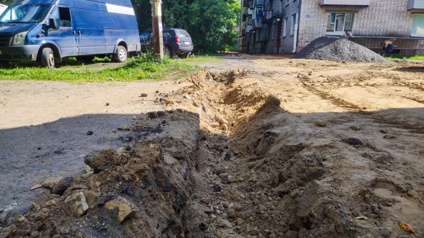 Разрытый дворовой проезд с траншеей и парковкой автомобилей рядом с многоэтажным домом