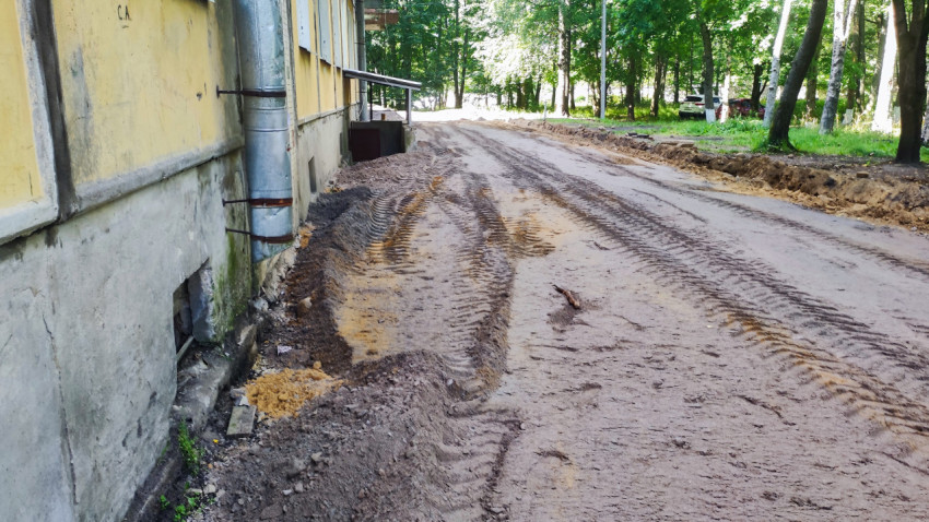 Грунтовый проезд вдоль фасада с водосточной трубой и траншеей на этапе дворового ремонта
