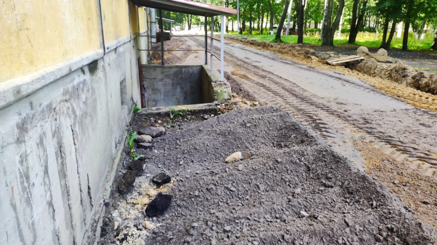 Проезд на ремонте рядом с цокольным входом и насыпью щебня у многоквартирного дома