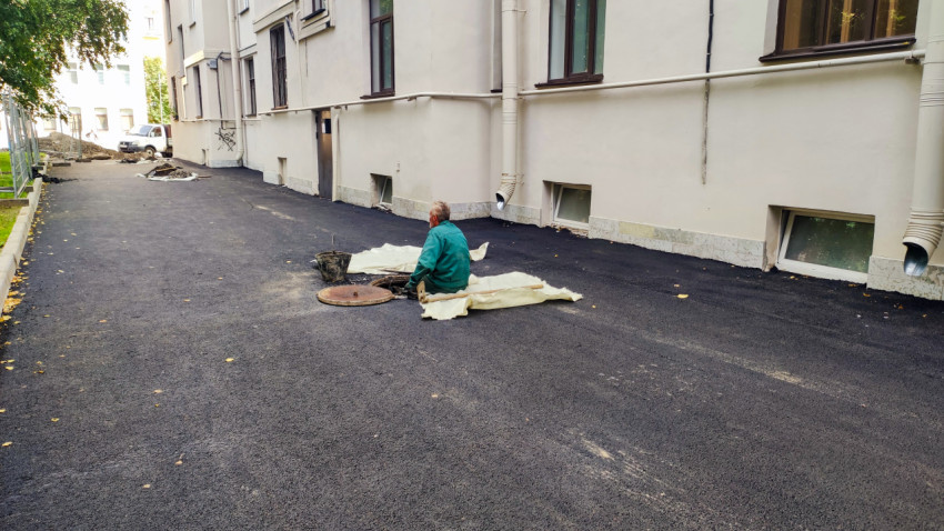 Рабочий у люка на свежем асфальте при ремонте внутридворового проезда