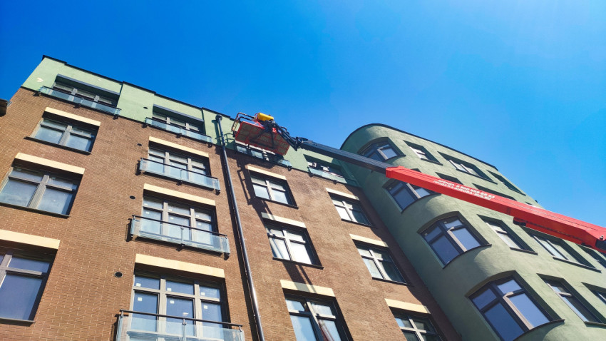 Рабочий в корзине автовышки выполняет фасадные работы у верхней части здания