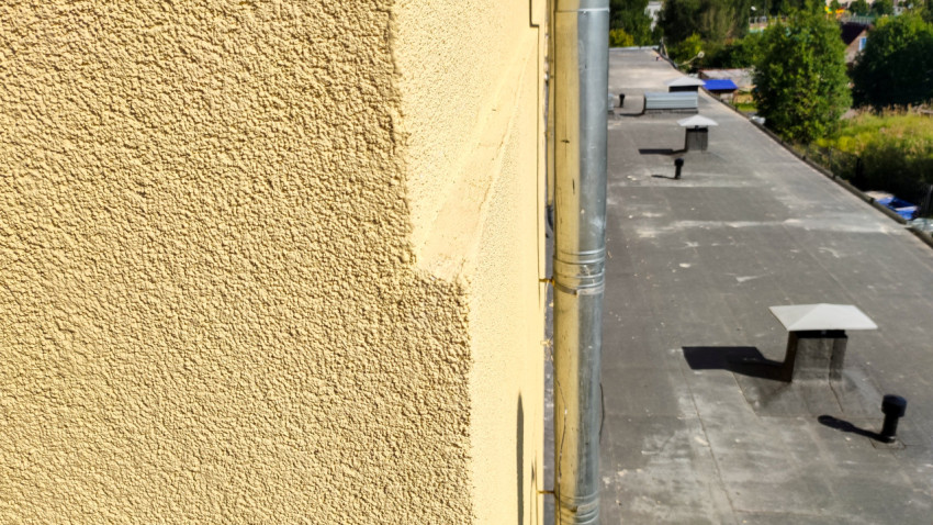 Фактурная фасадная штукатурка и водосточная труба у парапета плоской крыши здания