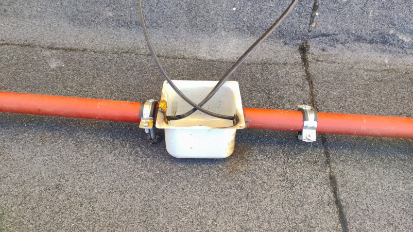 Красная труба с хомутами и открытой металлической коробкой для ввода кабелей на плоской кровле