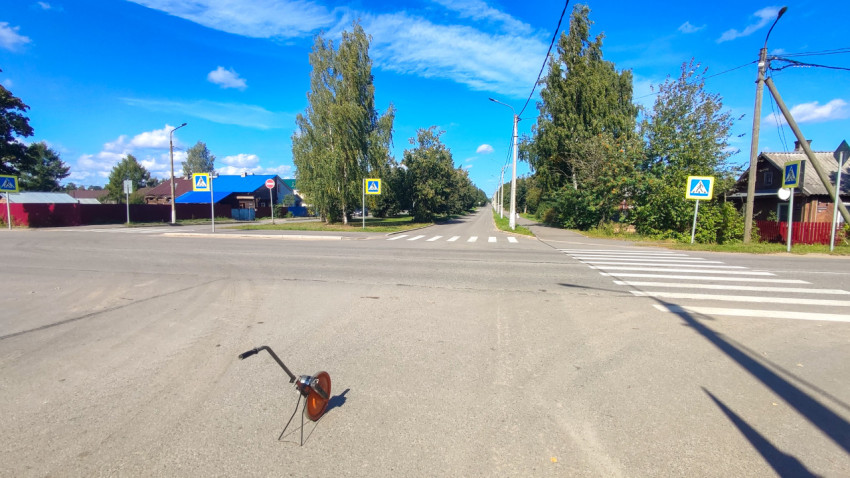 Измерительное колесо лежит на дороге у перекрёстка с пешеходным переходом и знаками