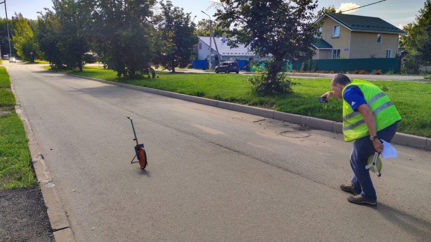 Рабочий снимает люк и участок асфальта рядом с бордюром, оставив измерительное колесо на дороге