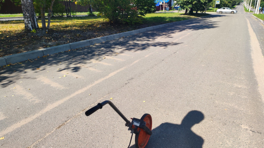 Измерительное колесо стоит на асфальте у тихой улицы с деревьями и бордюром