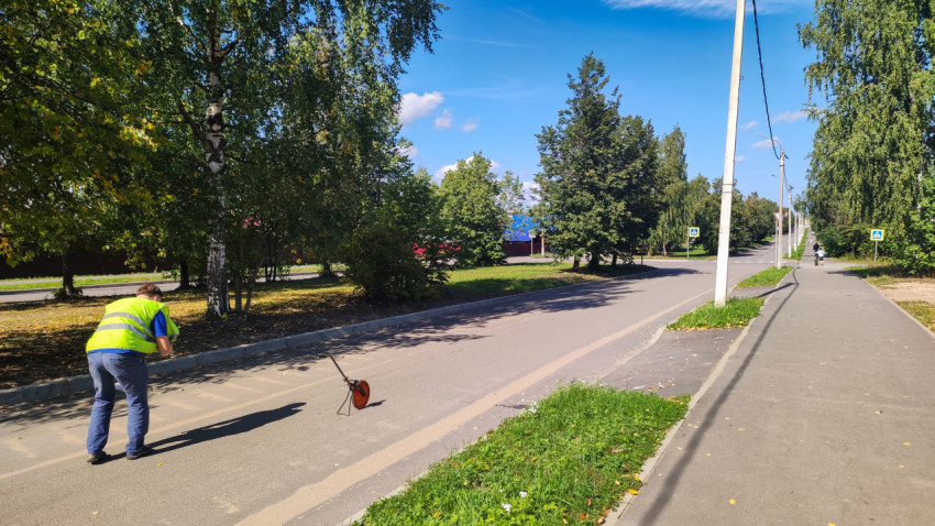 Рабочий в сигнальном жилете фотографирует измерительное колесо на асфальтовой дороге