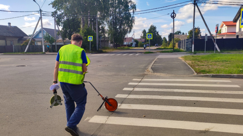 Рабочий с измерительным колесом проходит по зебре на перекрёстке