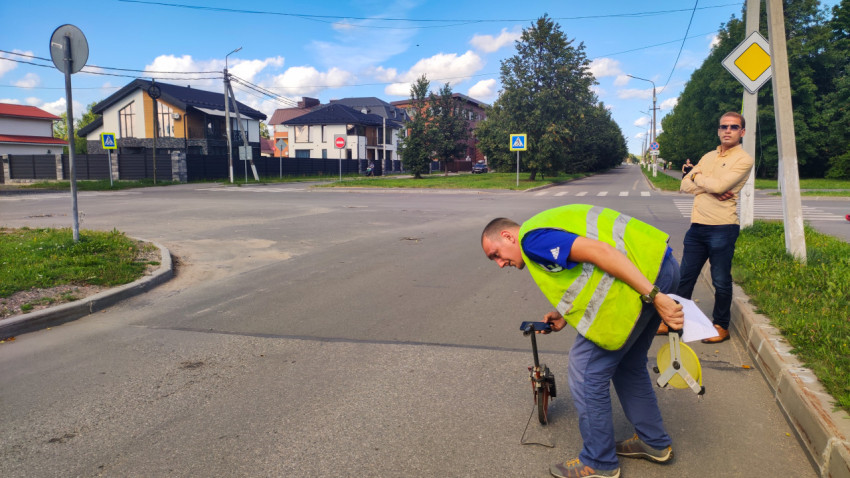 Двое мужчин на перекрёстке делают замеры дороги колесом и рулеткой