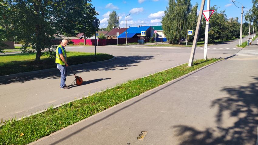 Специалист с измерительным колесом делает замеры у перекрёстка в жилом районе