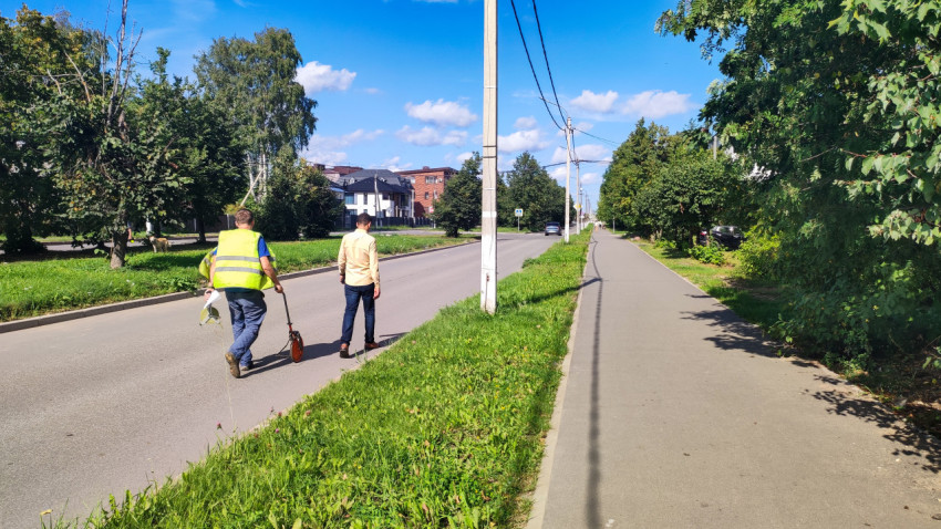 Два человека идут вдоль дороги, а рабочий тянет за собой измерительное колесо по обочине