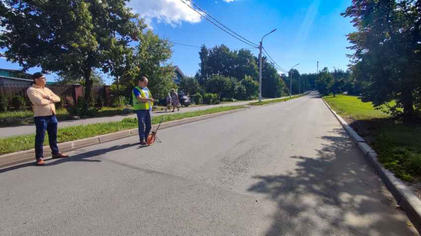 Дорожник с измерительным колесом и напарник стоят на пустой улице перед длинным прямым участком дороги