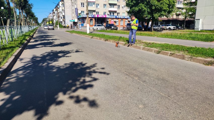 Дорожный рабочий с измерительным колесом у бордюра на улице с деревьями и жилыми домами