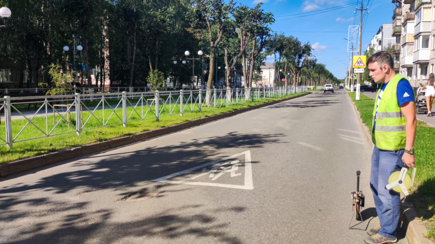 Сотрудник у дороги готовит замер, рядом знаки «дети» и пешеходного перехода