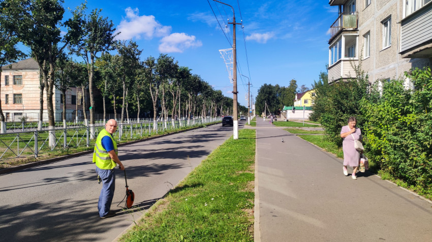 Дорожник с измерительным колесом идёт по улице, пока по тротуару проходит прохожая