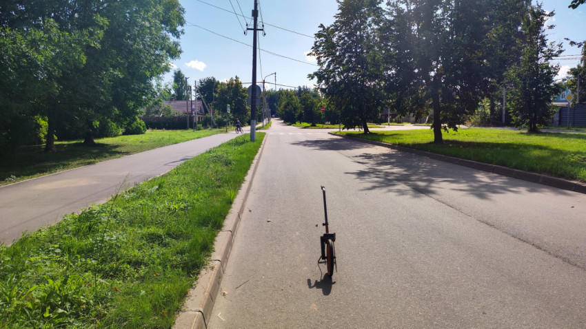 Измерительное колесо стоит посреди тихой улицы на фоне деревьев и частных домов