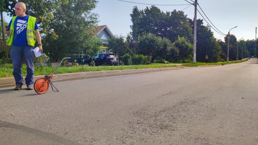 Парень в жилете меряет улицу измерительным колесом на пустой дороге